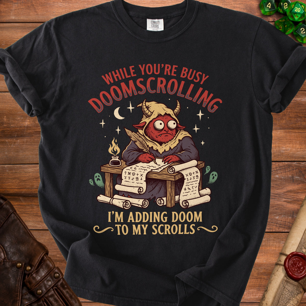 Black t-shirt with a devil writing scrolls, saying "While you're busy doomscrolling, I'm adding doom to my scrolls."
