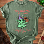 Green t-shirt with a cartoon goblin in a wizard hat holding a brick. Text reads "The crystal I'm using to protect my peace this year."