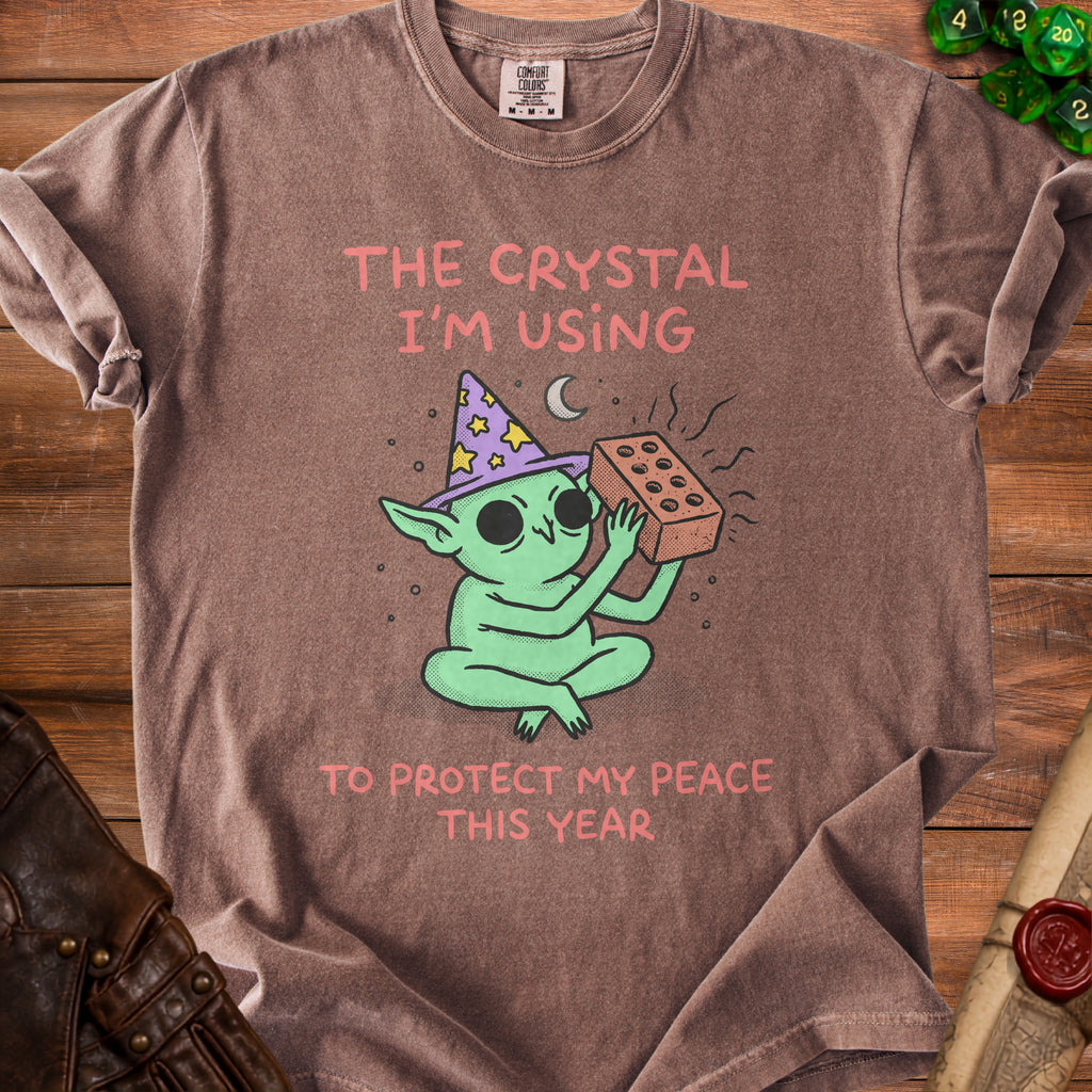 Brown t-shirt with cartoon wizard goblin holding a brick, saying "The crystal I'm using to protect my peace this year."