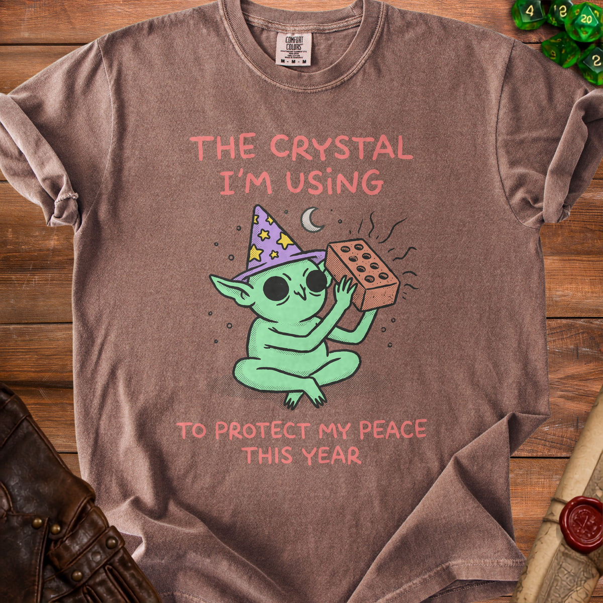 Brown t-shirt with cartoon wizard goblin holding a brick, saying "The crystal I'm using to protect my peace this year."