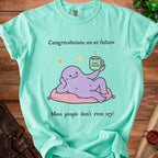 Light green t-shirt with a cartoon purple creature holding a mug labeled "Good Enough."