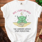 White t-shirt with green creature wishing for horrors to stop persisting.