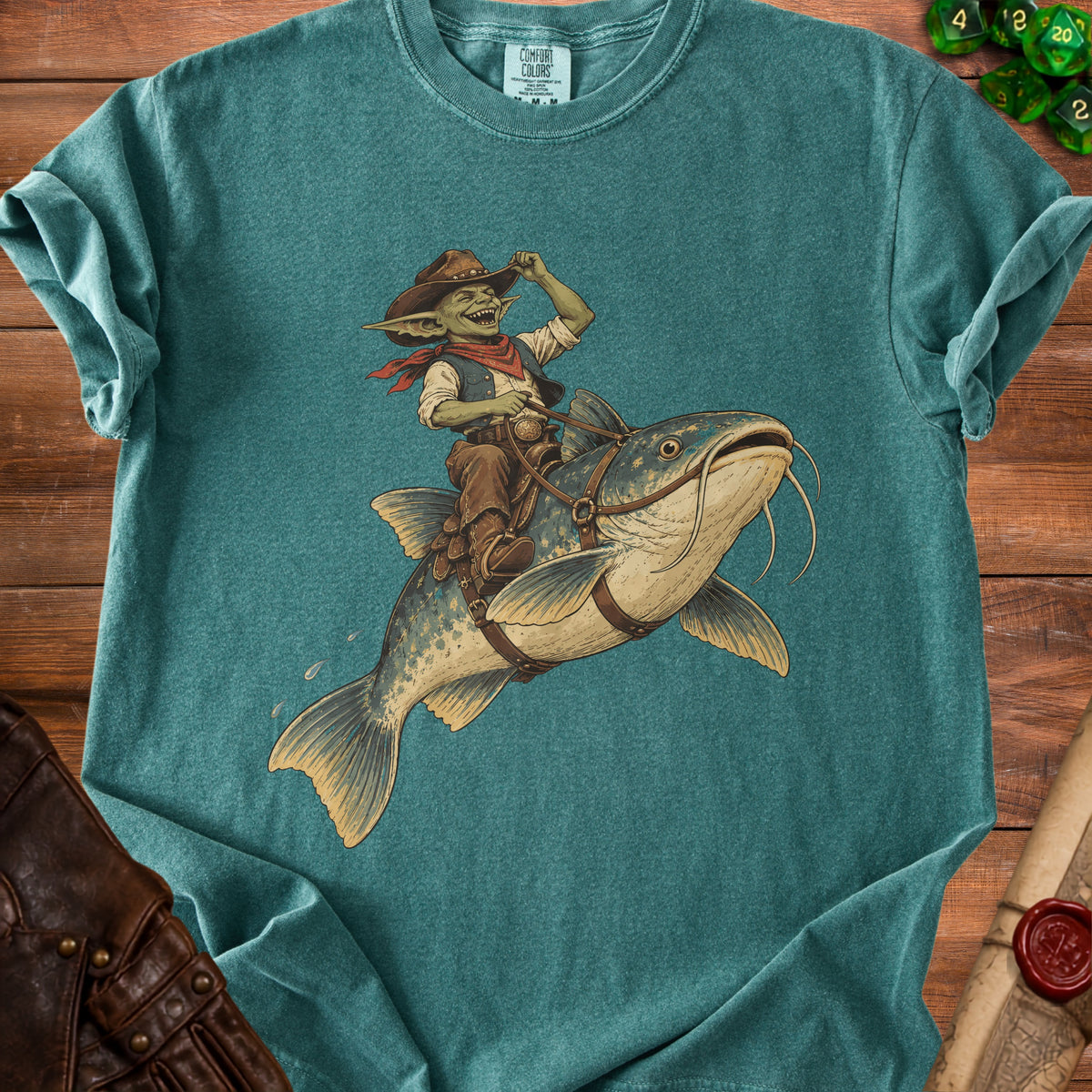Goblin cowboy riding a catfish on a teal t-shirt.