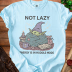 Light blue t-shirt with illustration of a creature in a blanket, text "NOT LAZY ENERGY IS IN HUDDLE MODE".