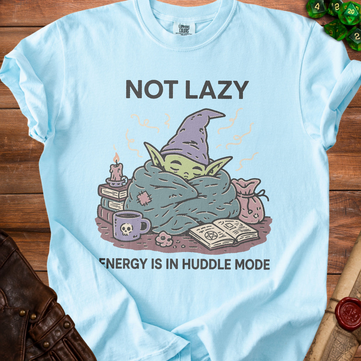 Light blue t-shirt with illustration of a creature in a blanket, text "NOT LAZY ENERGY IS IN HUDDLE MODE".