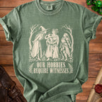 Green t-shirt with white graphic of three women, a mushroom, and text "OUR HOBBIES REQUIRE WITNESSES".