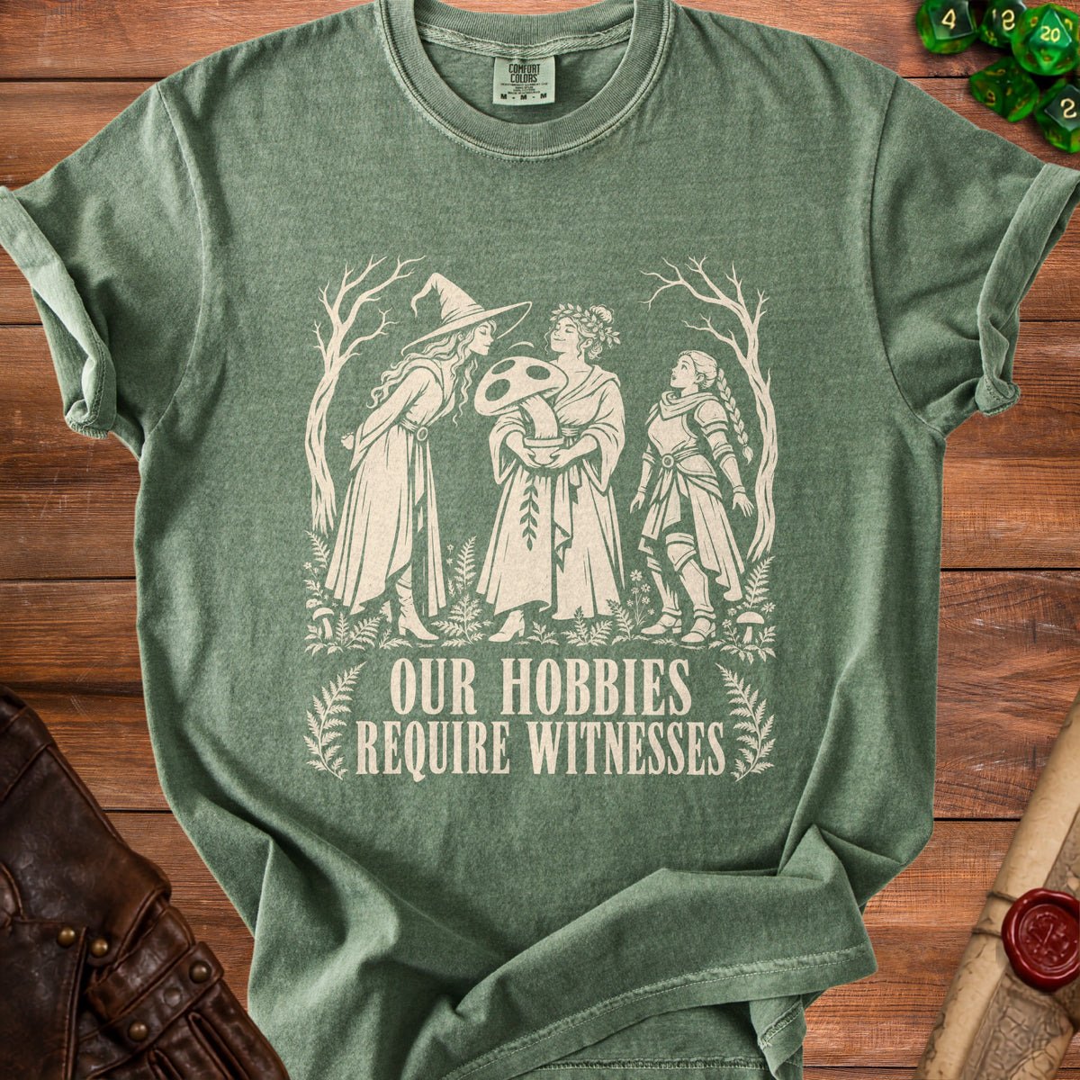 Green t-shirt with white graphic of three women, a mushroom, and text "OUR HOBBIES REQUIRE WITNESSES".