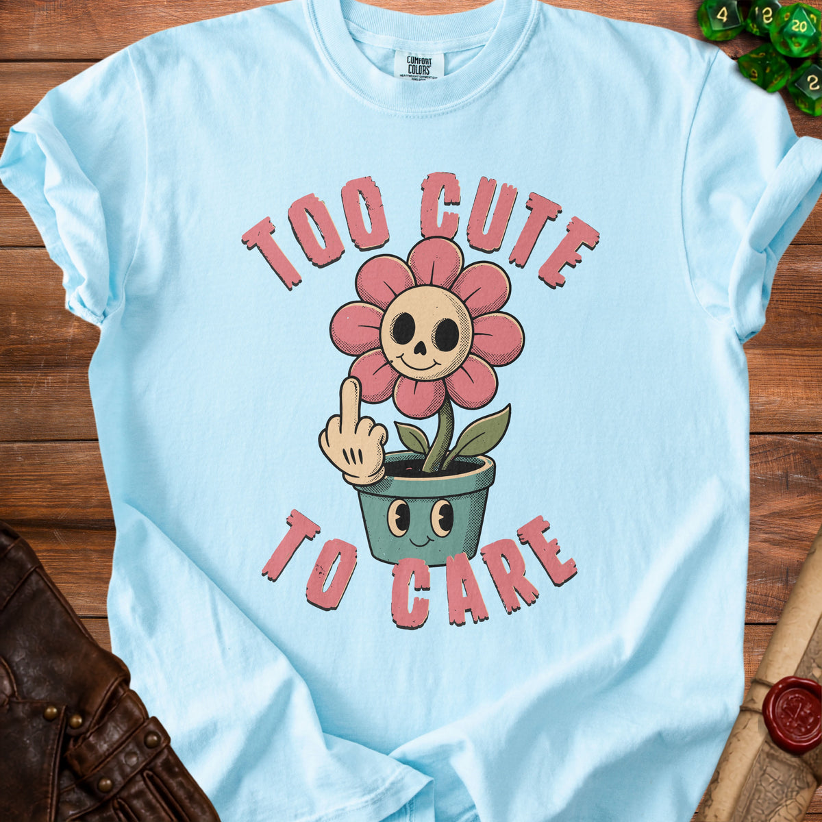 Light blue t-shirt with a cartoon flower with skull face saying "Too cute to care".