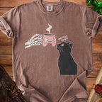 Skeleton hand holds game controller mug, black cat looks up and reads "One More Game?".