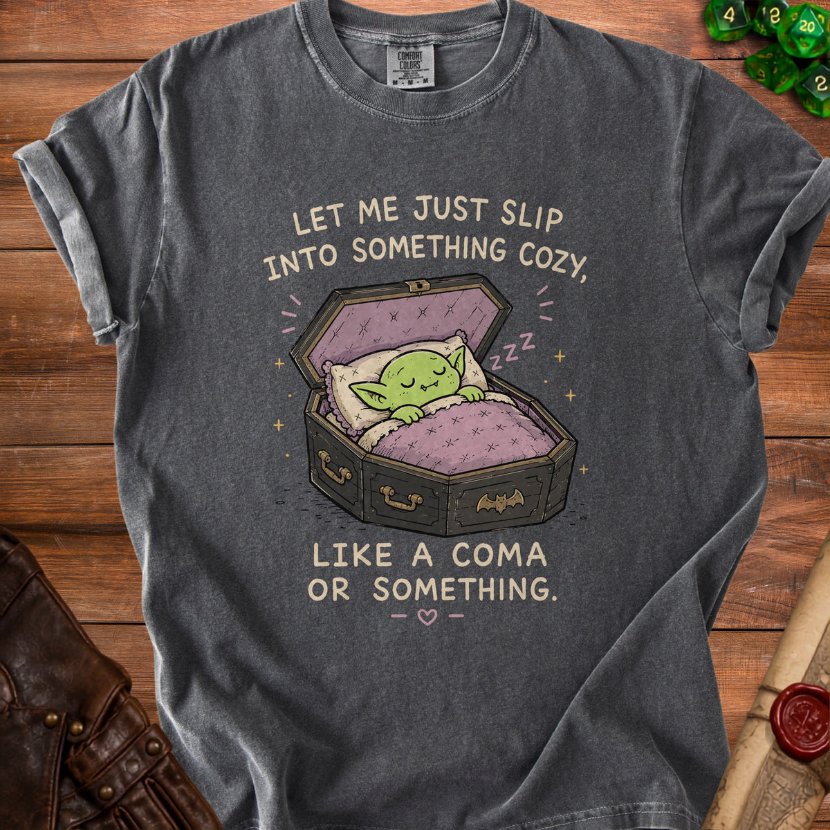 Gray t-shirt with a green goblin sleeping in a coffin and text that reads "Let me just slip into something cozy, like a coma or something."