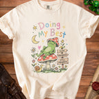 Cream t-shirt with graphic of frog on mushroom, snail, moon, and text "Doing My Best".
