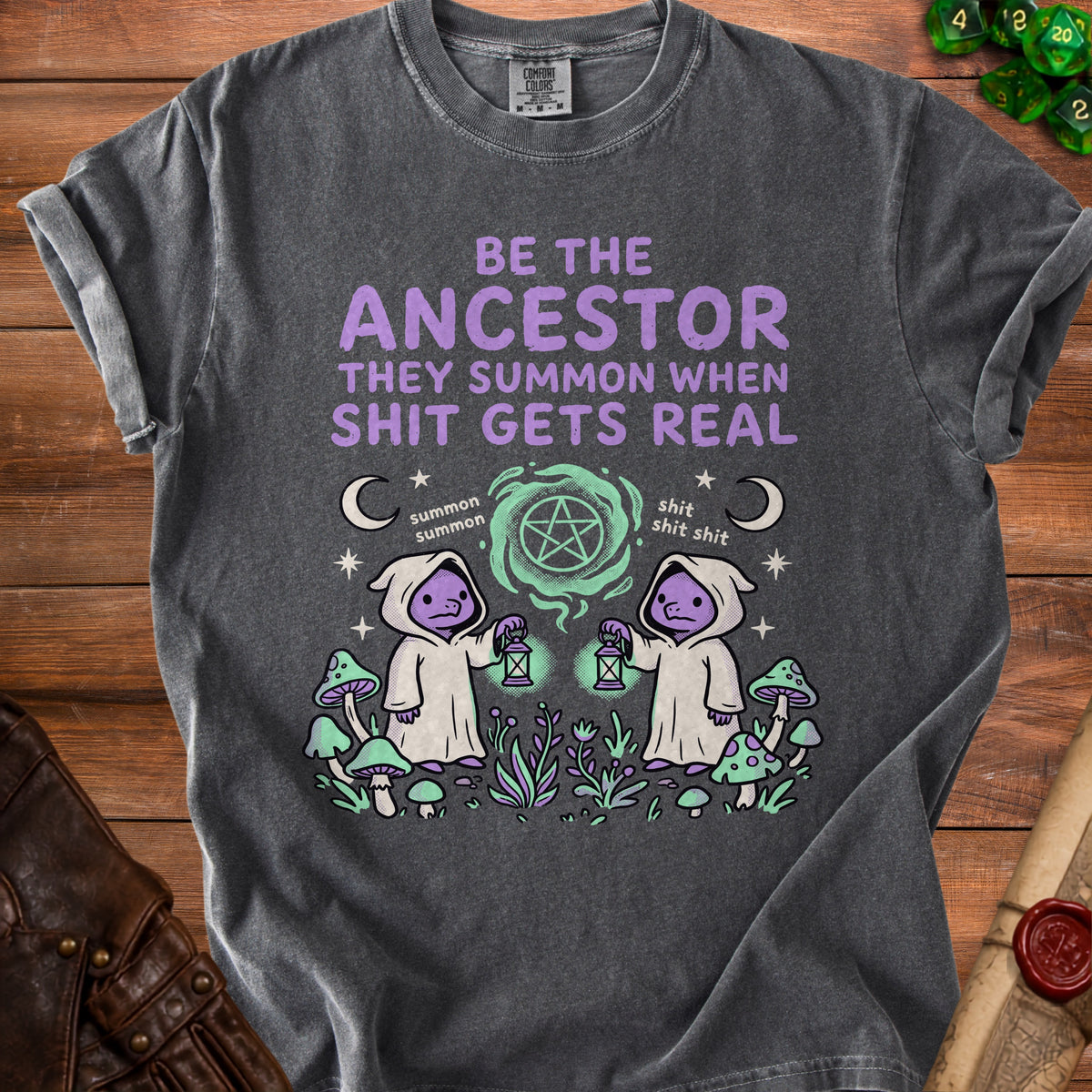 Dark gray t-shirt with purple text "Be the Ancestor They Summon When Shit Gets Real." and cartoon figures.