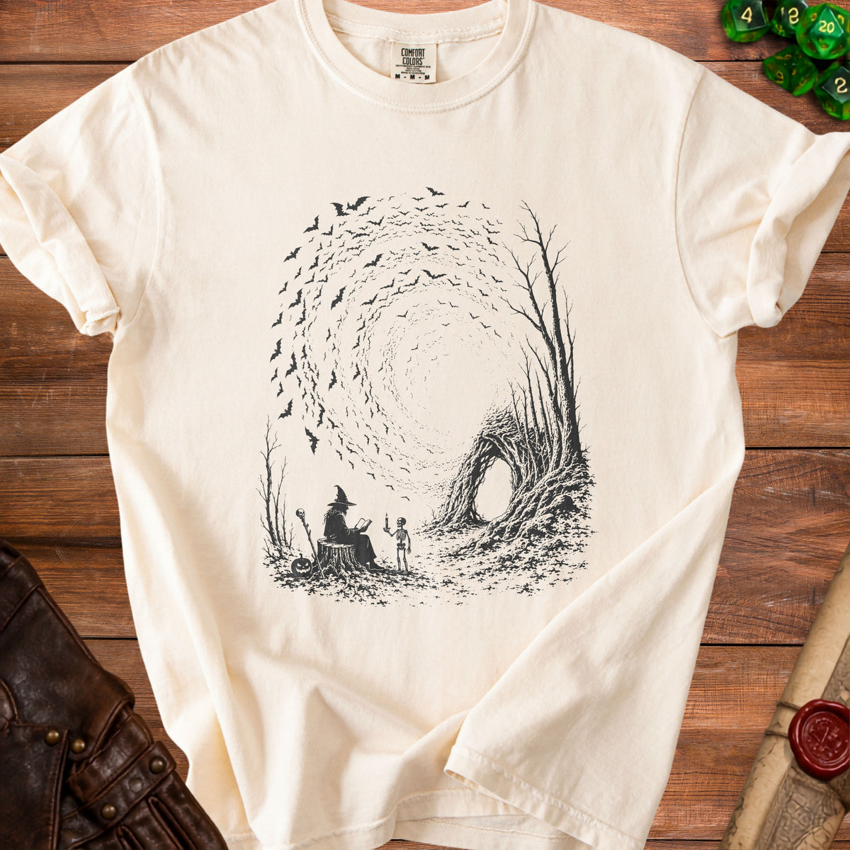Cream t-shirt with black graphic of witch, skeleton, bats, and hollow tree entrance.
