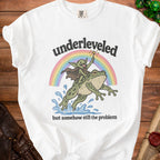 White t-shirt with graphic of goblin riding frog under rainbow with text "underleveled but somehow still the problem".
