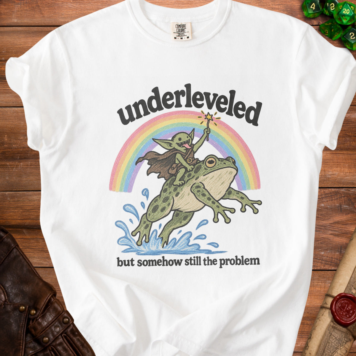 White t-shirt with graphic of goblin riding frog under rainbow with text "underleveled but somehow still the problem".