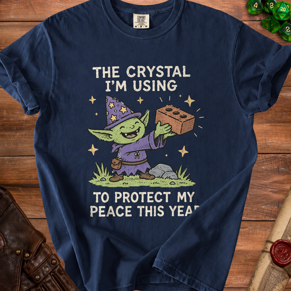 Navy t-shirt with graphic of a smiling goblin wizard holding a brick, text reads "The crystal I'm using to protect my peace this year."
