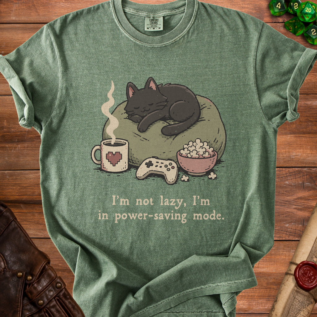 Green t-shirt with illustration of sleeping cat, coffee, popcorn, and game controller. Text reads "I'm not lazy, I'm in power-saving mode."