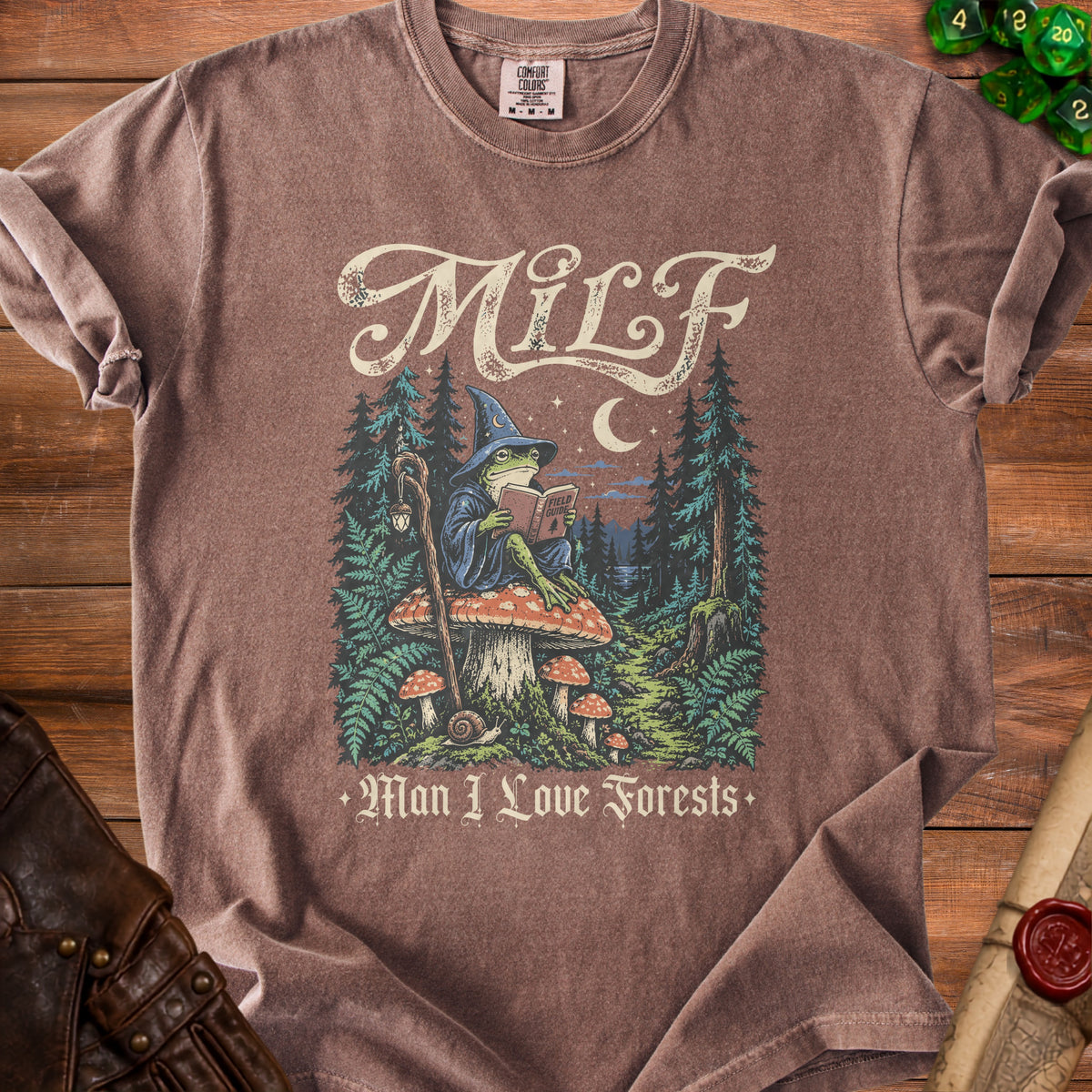 Brown t-shirt with a graphic of a wizard frog reading a book titled "Field Guide" in a forest.
