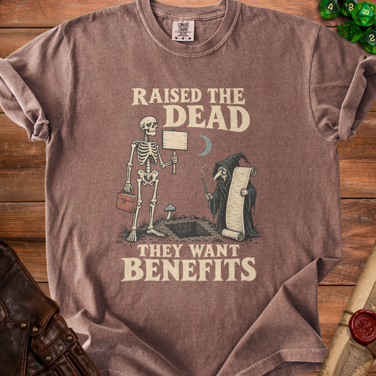 T-shirt with skeleton holding sign and grim reaper reading scroll, text "Raised the Dead, They Want Benefits".