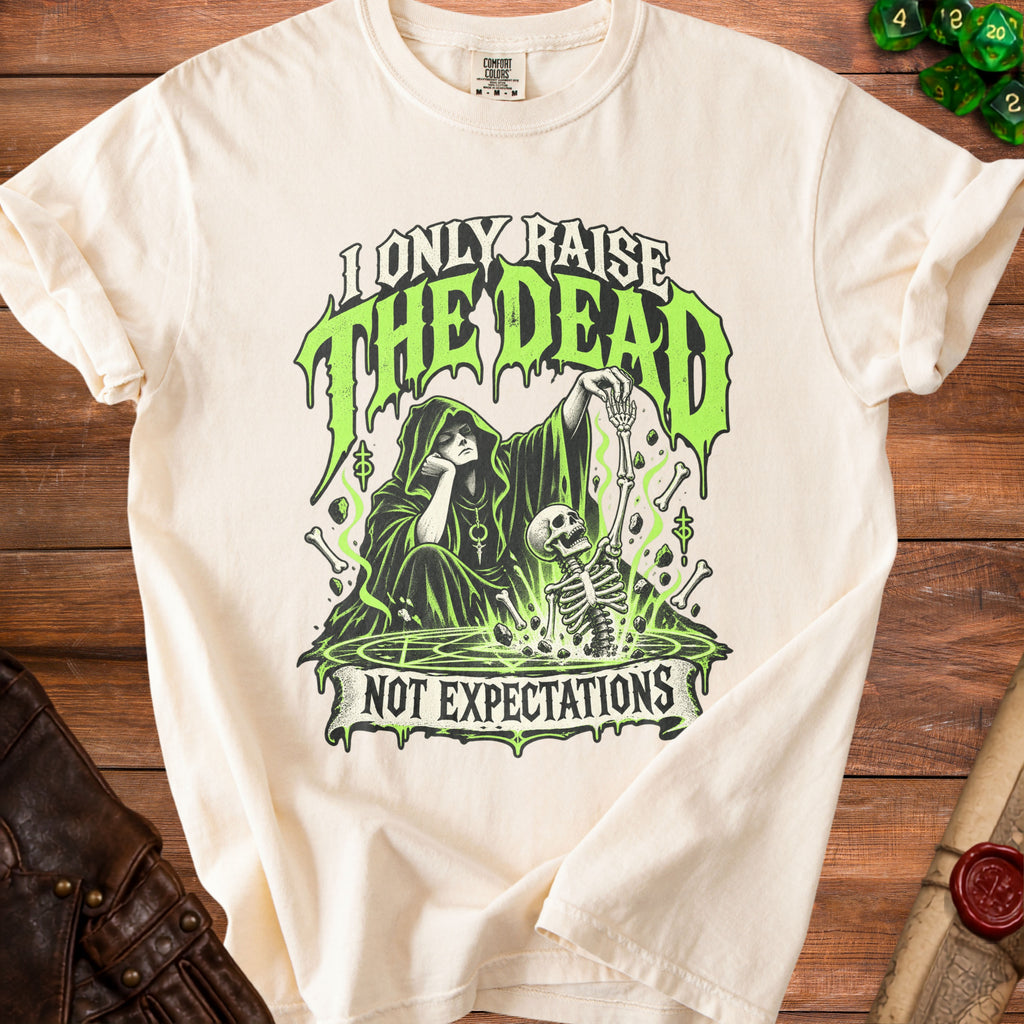Cream t-shirt with graphic of a grim reaper and skeleton, "I ONLY RAISE THE DEAD NOT EXPECTATIONS" text.