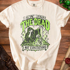 Cream t-shirt with graphic of a grim reaper and skeleton, "I ONLY RAISE THE DEAD NOT EXPECTATIONS" text.