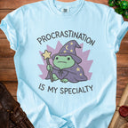 Light blue t-shirt with a frog wizard graphic and text "Procrastination is my specialty".