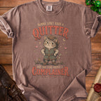 Brown t-shirt with a cartoon cat wearing a hat and tunic, stating "Momma didn't raise a quitter but she sure raised a complainer."