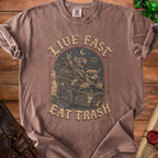 Brown t-shirt with graphic of cartoon rats in a cart with text "LIVE FAST EAT TRASH".