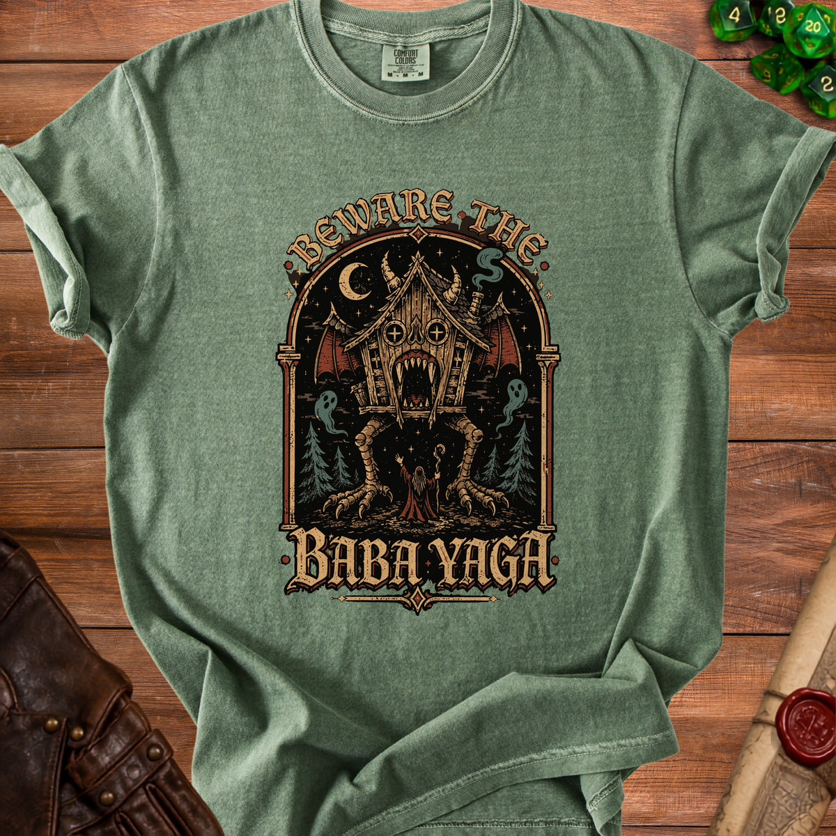 Green t-shirt with "Beware The Baba Yaga" text and illustration of a spooky cabin.