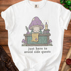 White t-shirt with illustration of a mushroom character reading a scroll, text "just here to avoid side quests".