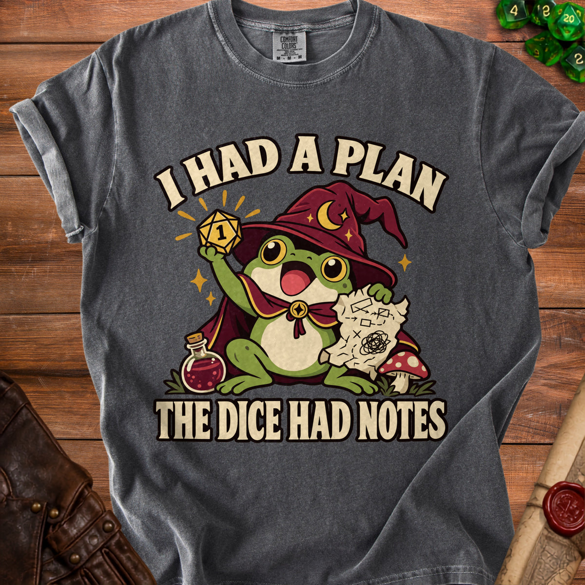 Dark gray t-shirt featuring a graphic of a frog wizard holding a critical fail die, potion, and map, with the text I HAD A PLAN THE DICE HAD NOTES.