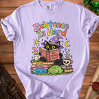 Black cat in witch hat reads book "But Books Help" on stack of books with frog.