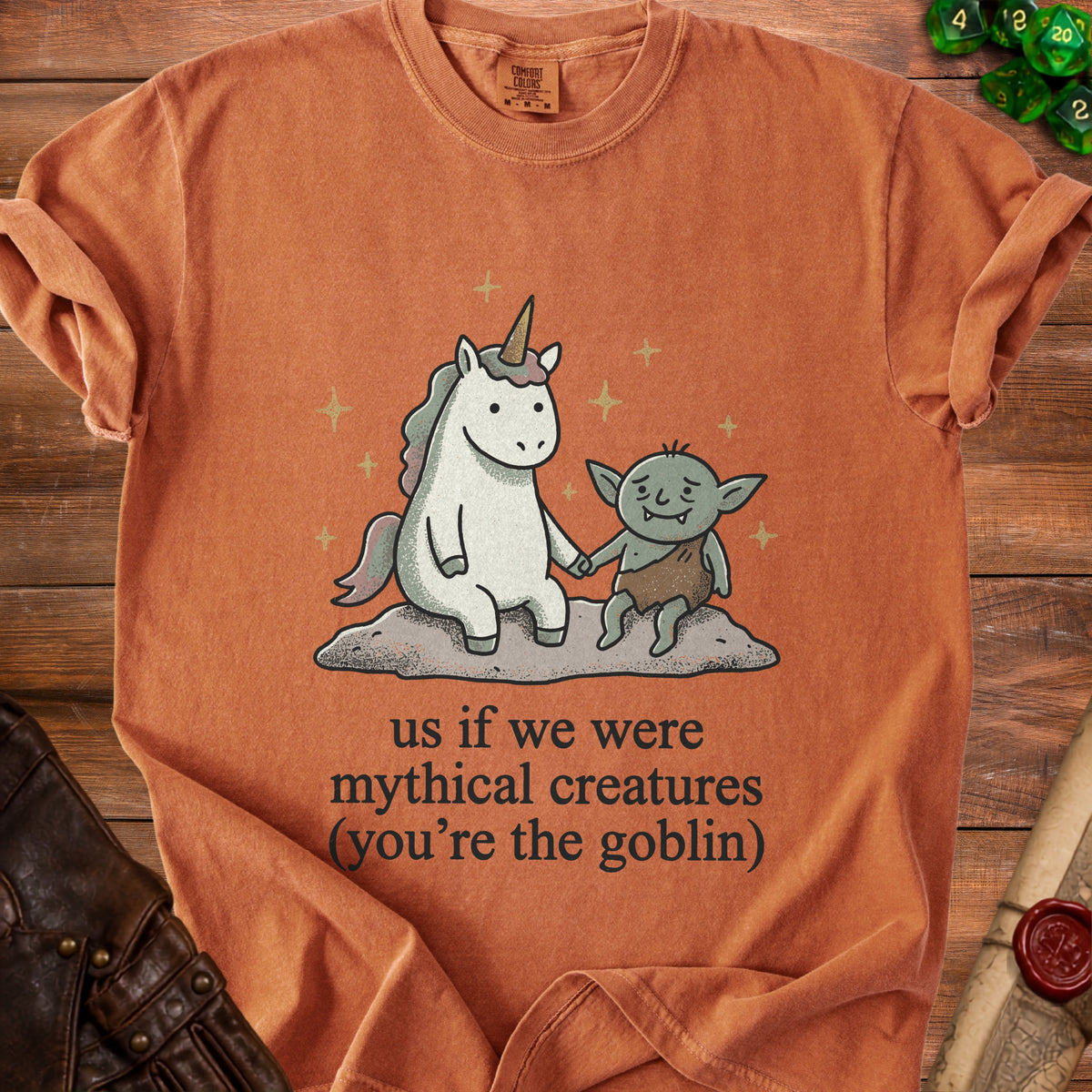 Orange t-shirt with unicorn and goblin graphic and text "us if we were mythical creatures".