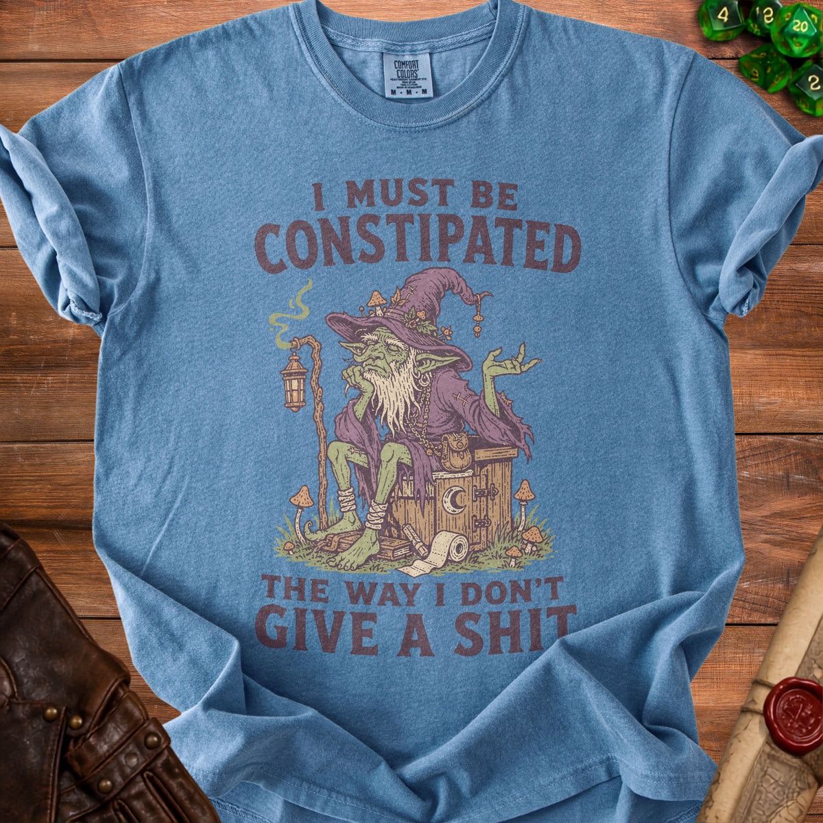 Blue t-shirt with illustration of a goblin witch on a toilet with text "I must be constipated".