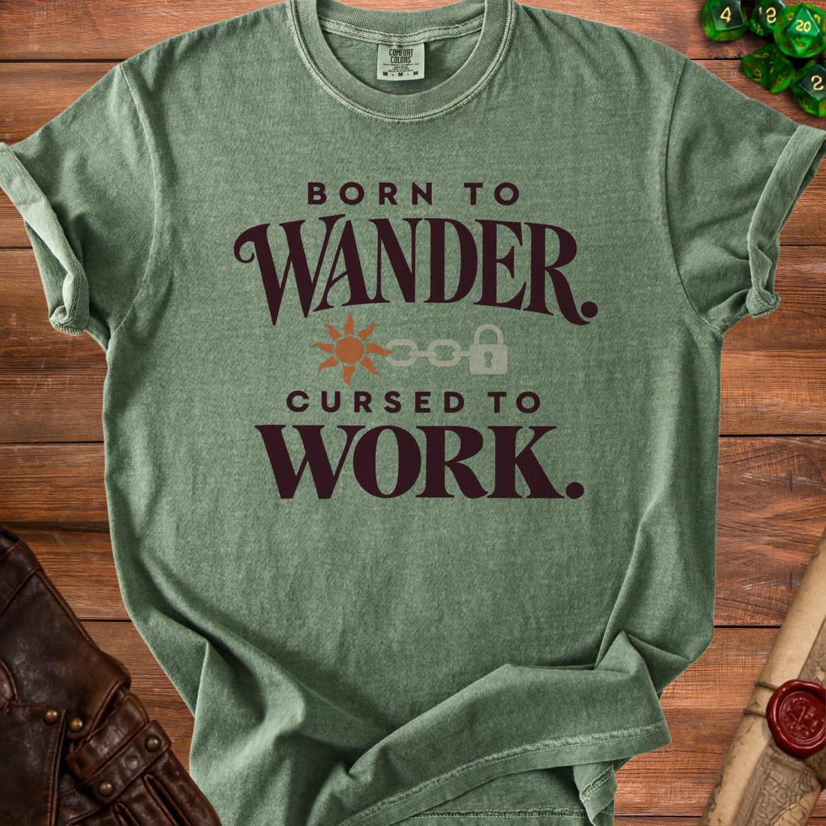 Green t-shirt with "Born to Wander, Cursed to Work" text and sun, chain, lock graphic.