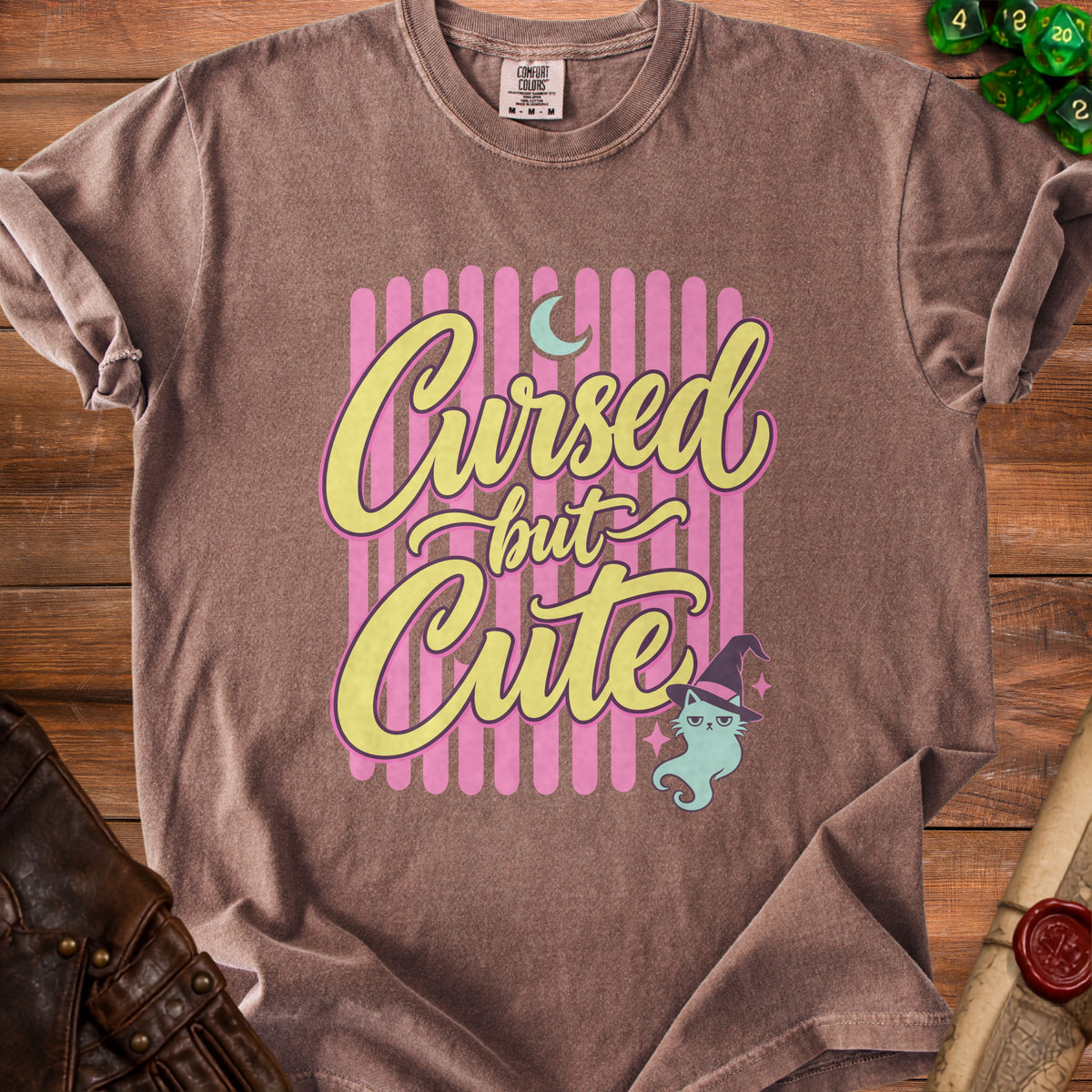 Brown t-shirt with "Cursed but Cute" text, a cat, and dice.