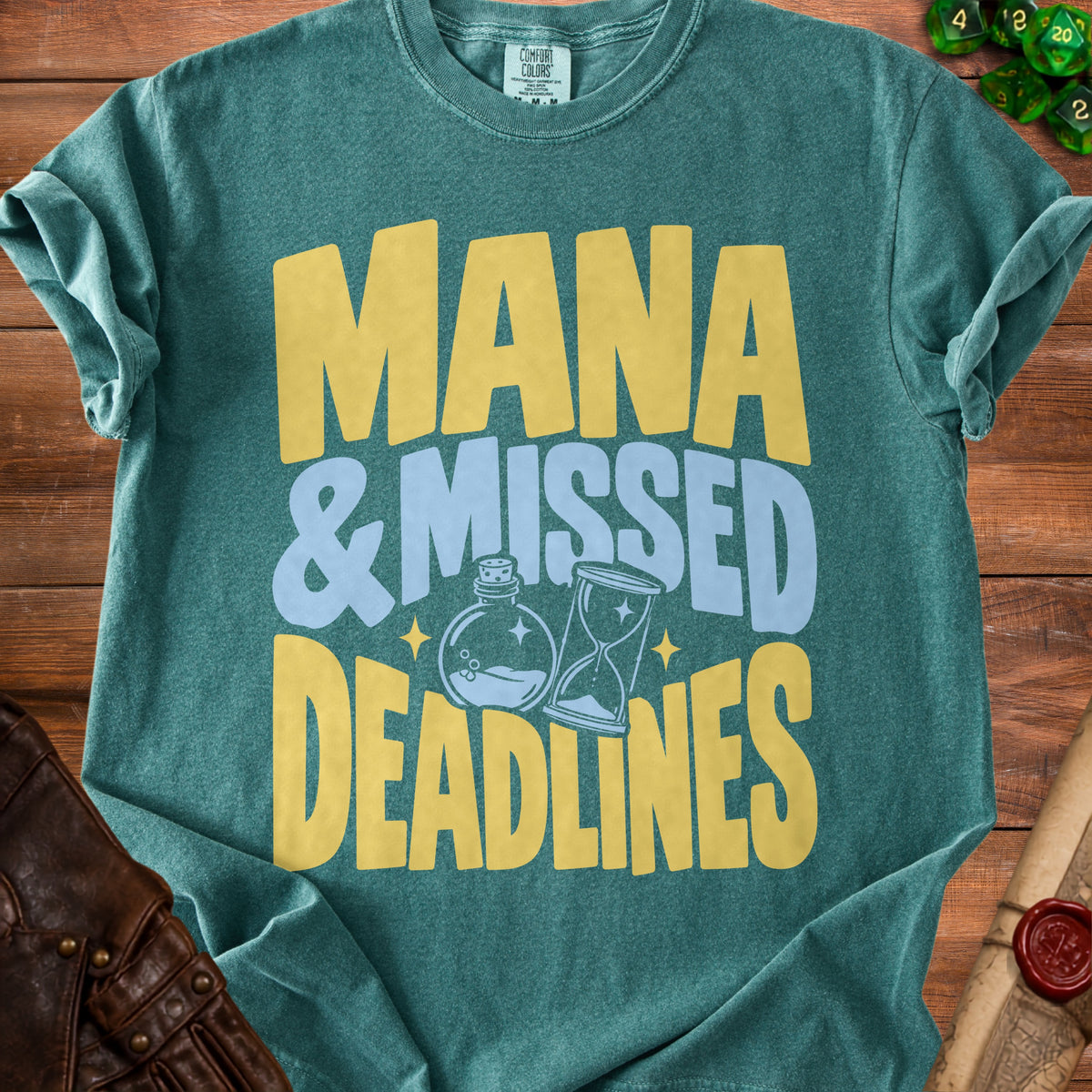 Teal t-shirt with yellow and blue text reading "MANA & MISSED DEADLINES" and icons.
