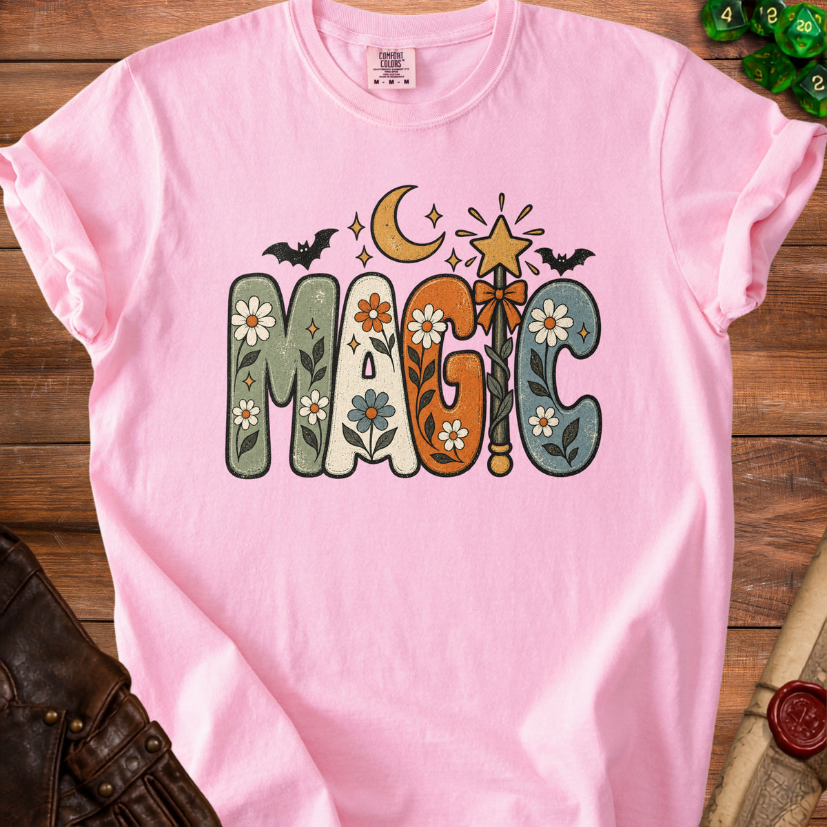 Pink t-shirt with "MAGIC" text in groovy font with floral and celestial designs.