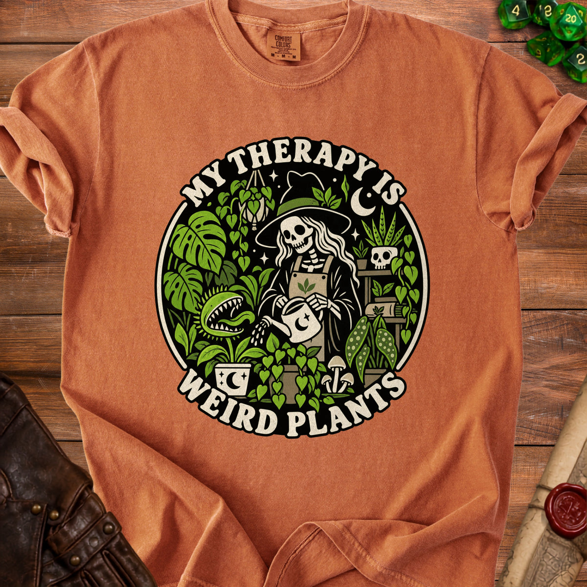 Orange t-shirt with a skeleton in a witch hat watering plants, text "MY THERAPY IS WEIRD PLANTS".