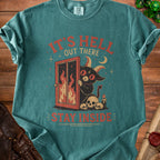 Graphic tee with a cartoon devil peeking through a fiery door, skulls, and text "It's hell out there, stay inside."