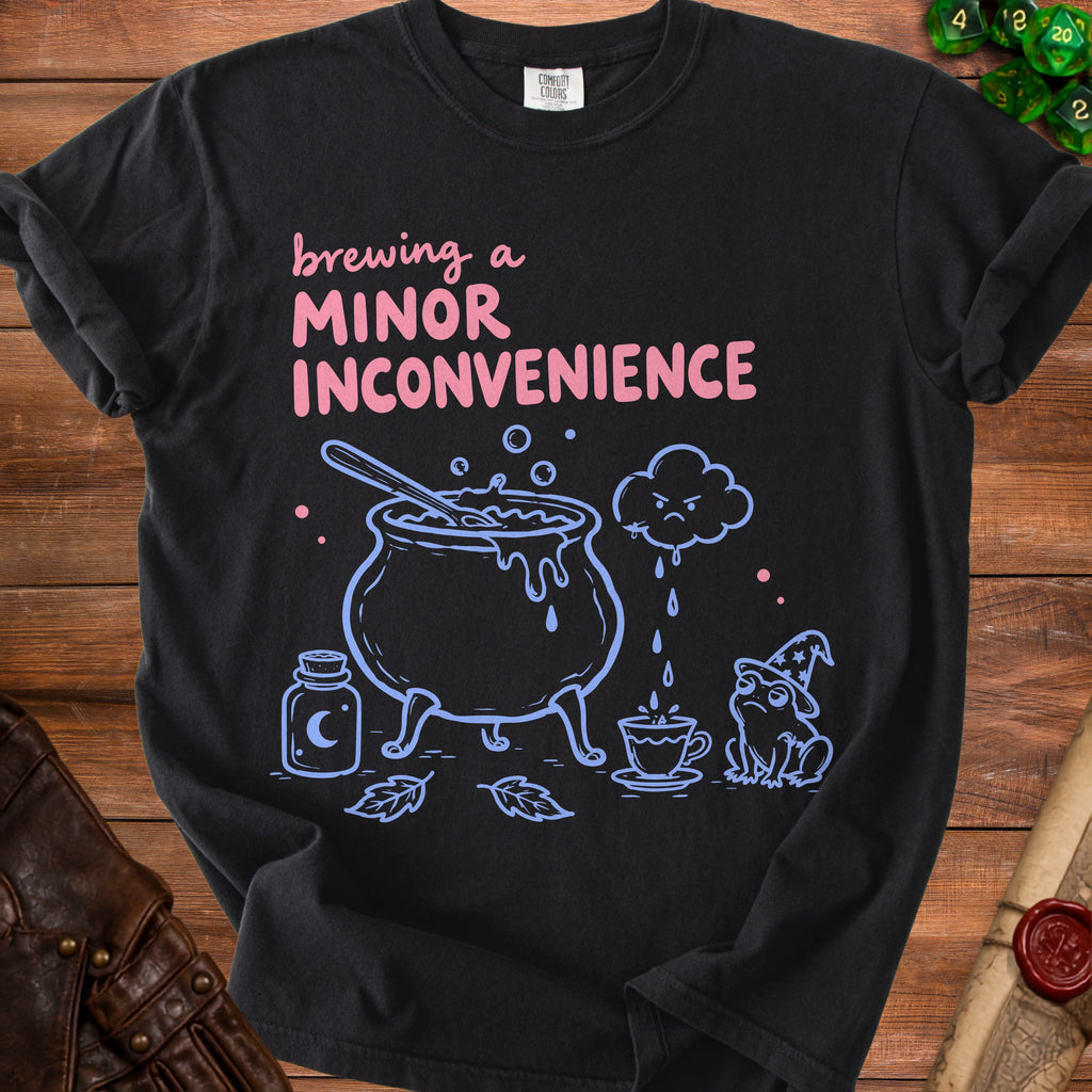 Black t-shirt with "brewing a minor inconvenience" text, cauldron, frog, and potion.
