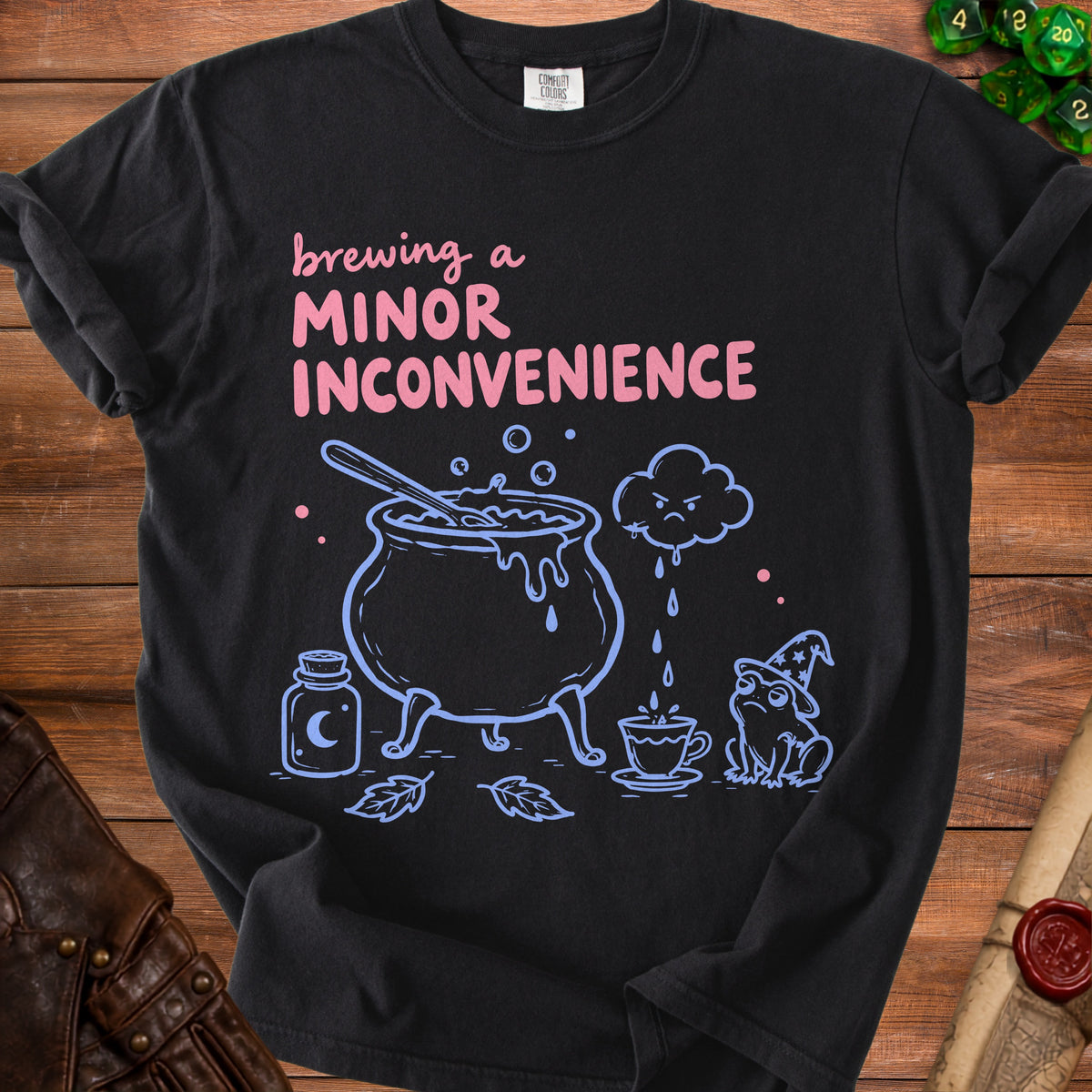 Black t-shirt with "brewing a minor inconvenience" text, cauldron, frog, and potion.