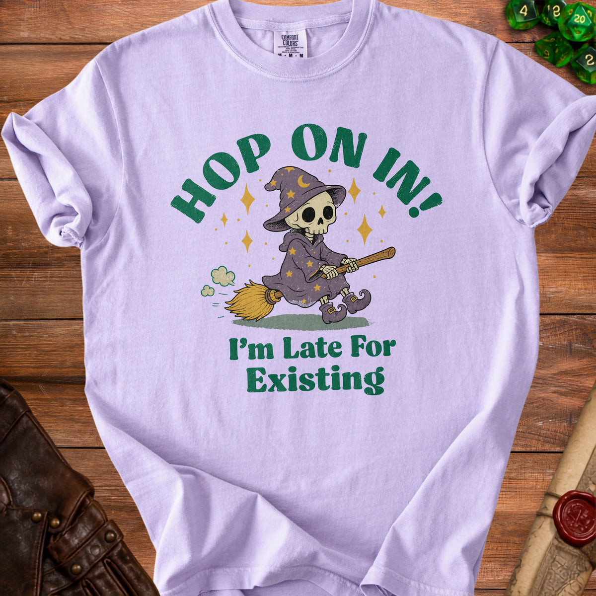 Lilac t-shirt with a skeleton wizard on a broom and text "Hop On In! I'm Late For Existing."