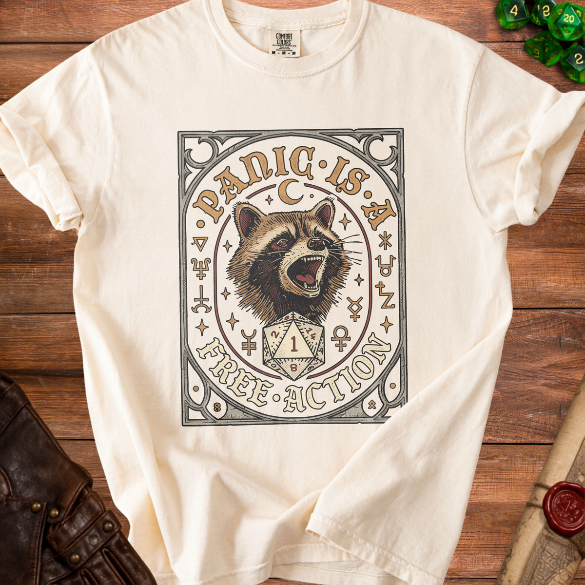 Cream t-shirt with a graphic of a raccoon, a d20 die, and the text "Panic is a Free Action".