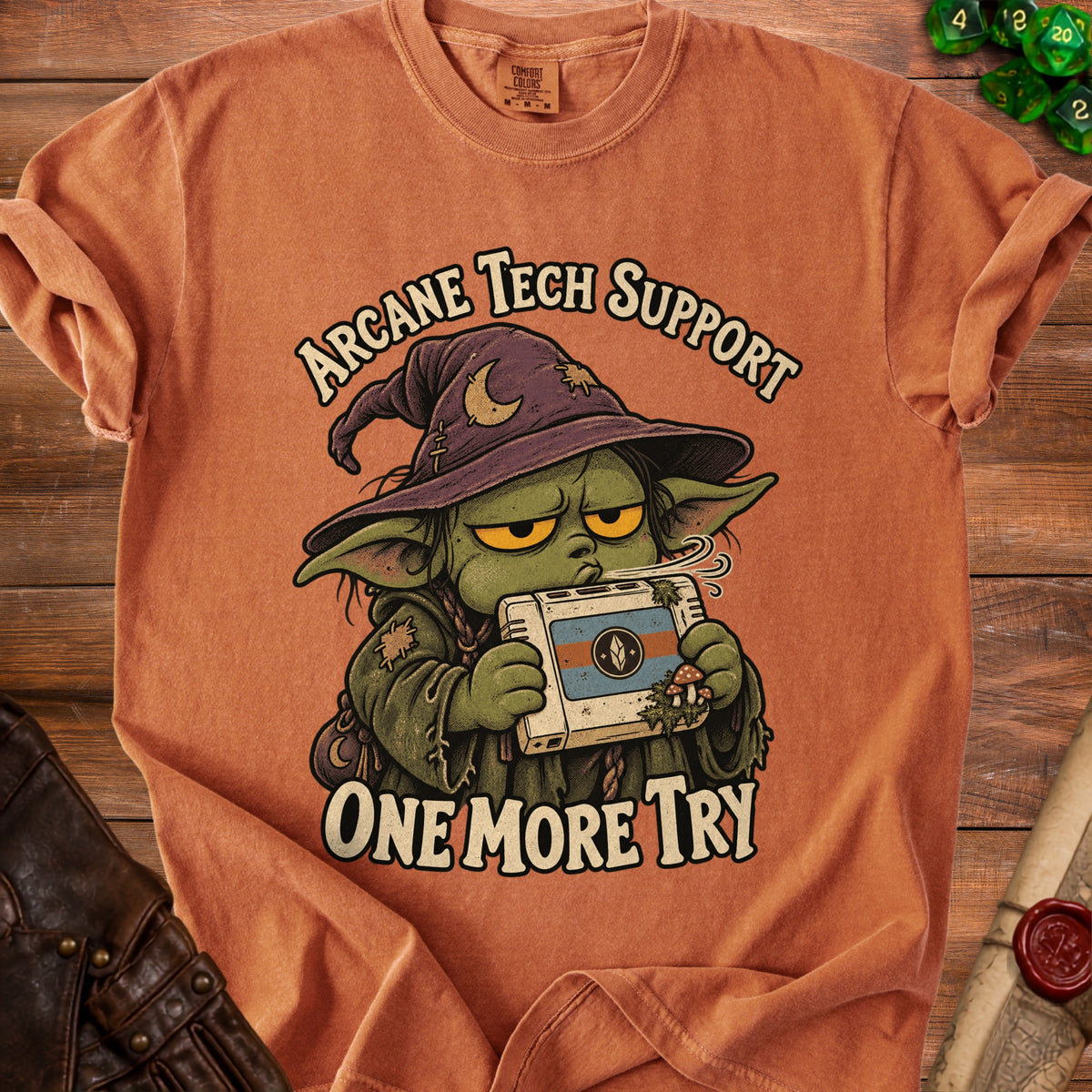 T-shirt with green goblin wizard character holding a retro console and text "Arcane Tech Support One More Try".