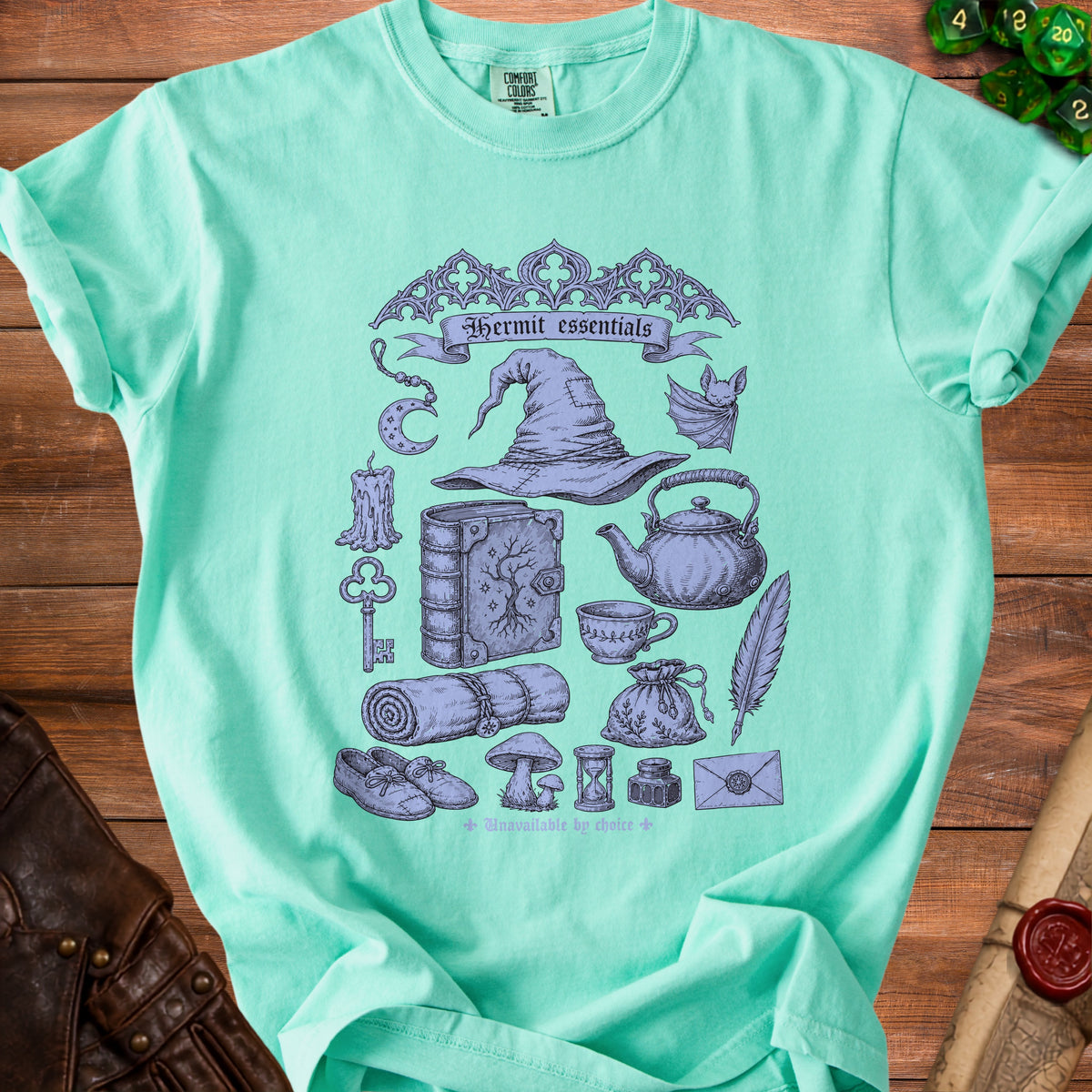 Light green t-shirt with purple illustration of witch's hat, book, and other magical items.