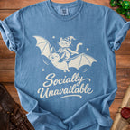 Blue t-shirt with white graphic of cat riding bat, "Socially Unavailable" text.
