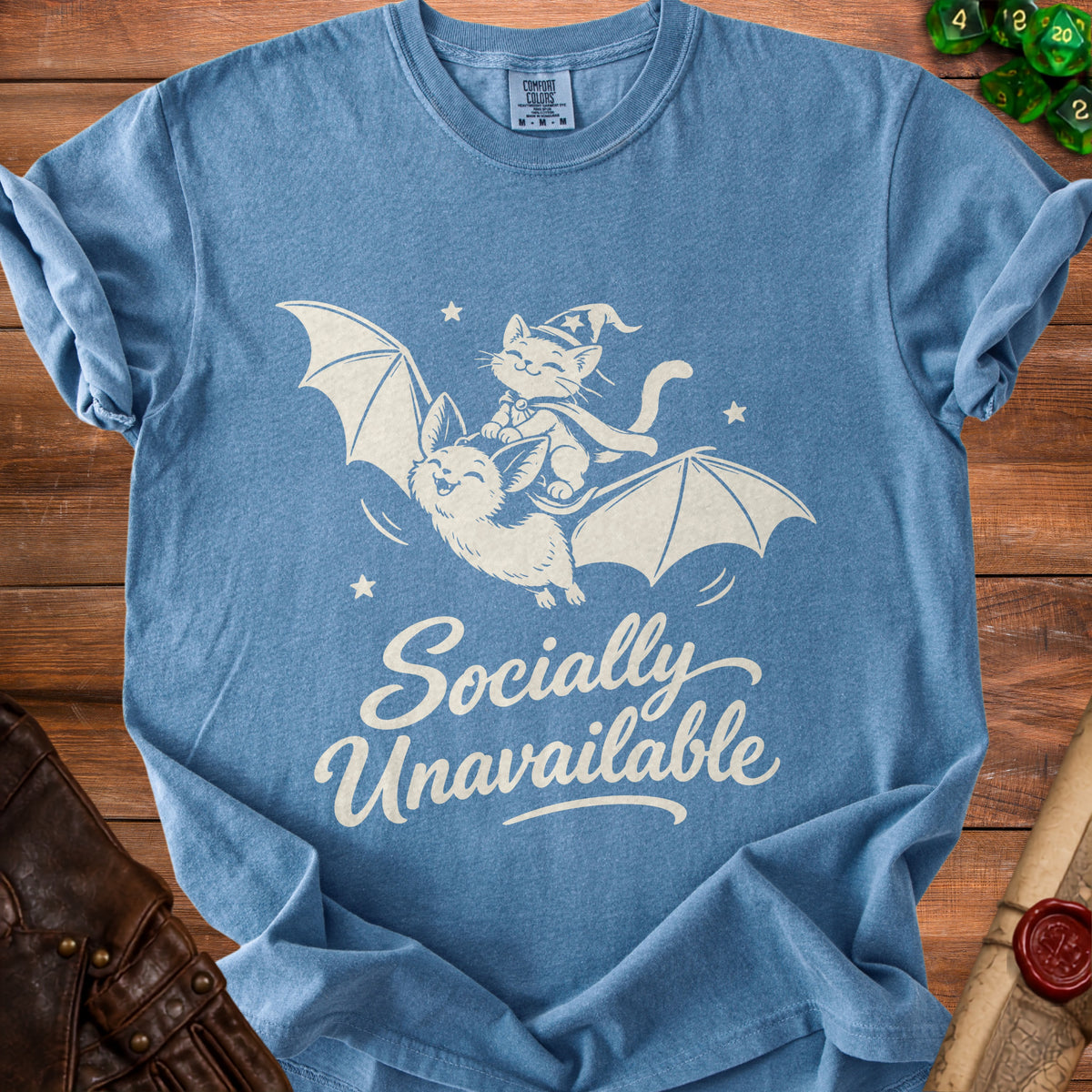 Blue t-shirt with white graphic of cat riding bat, "Socially Unavailable" text.