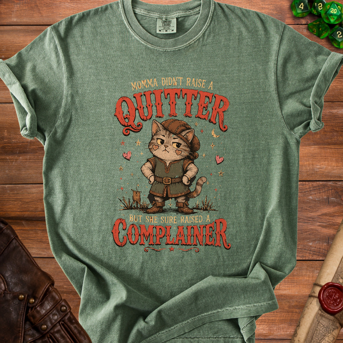 Green t-shirt with cat in medieval outfit saying "Momma didn't raise a quitter, but she sure raised a complainer."