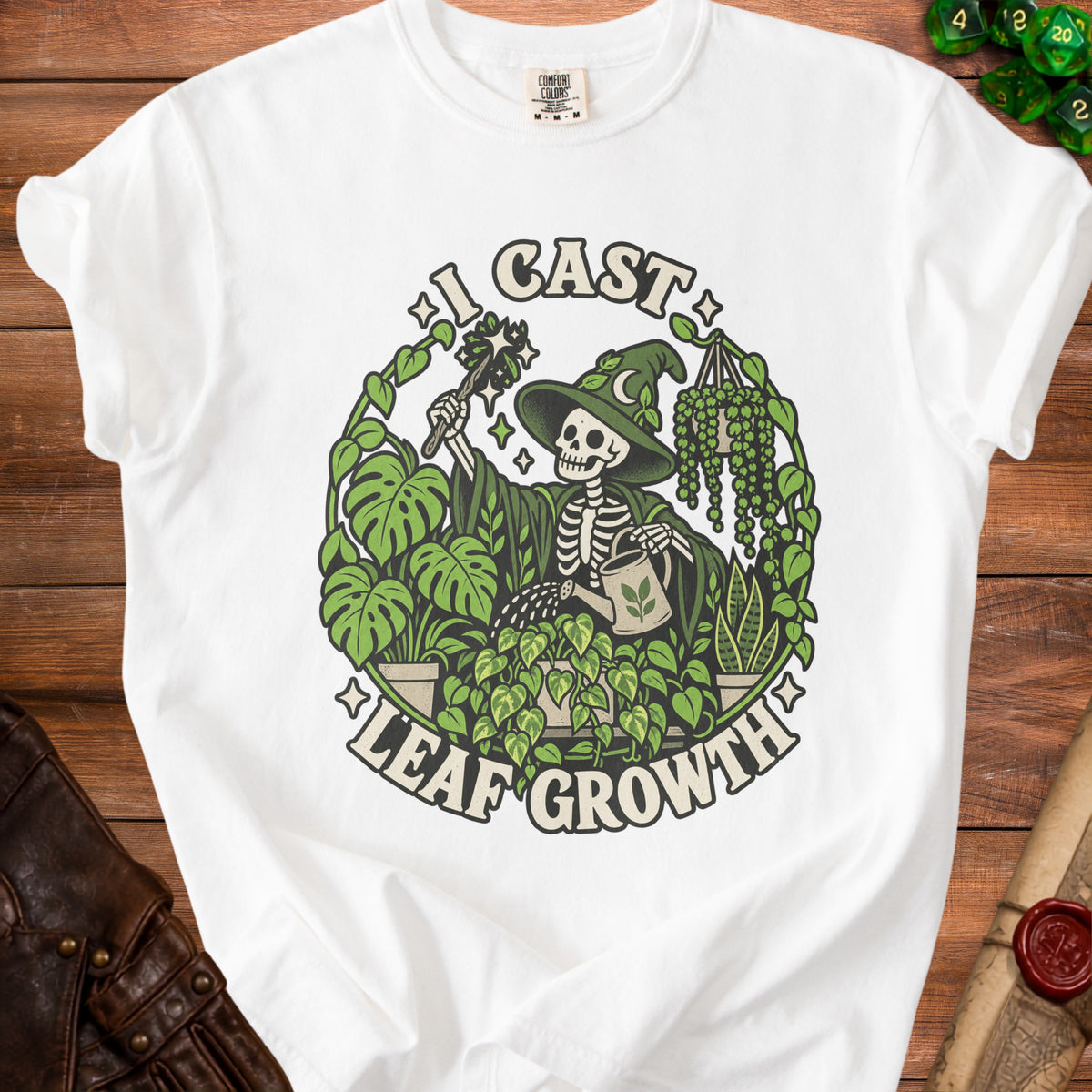 White t-shirt with graphic of skeleton witch watering plants, text reads "I CAST LEAF GROWTH".